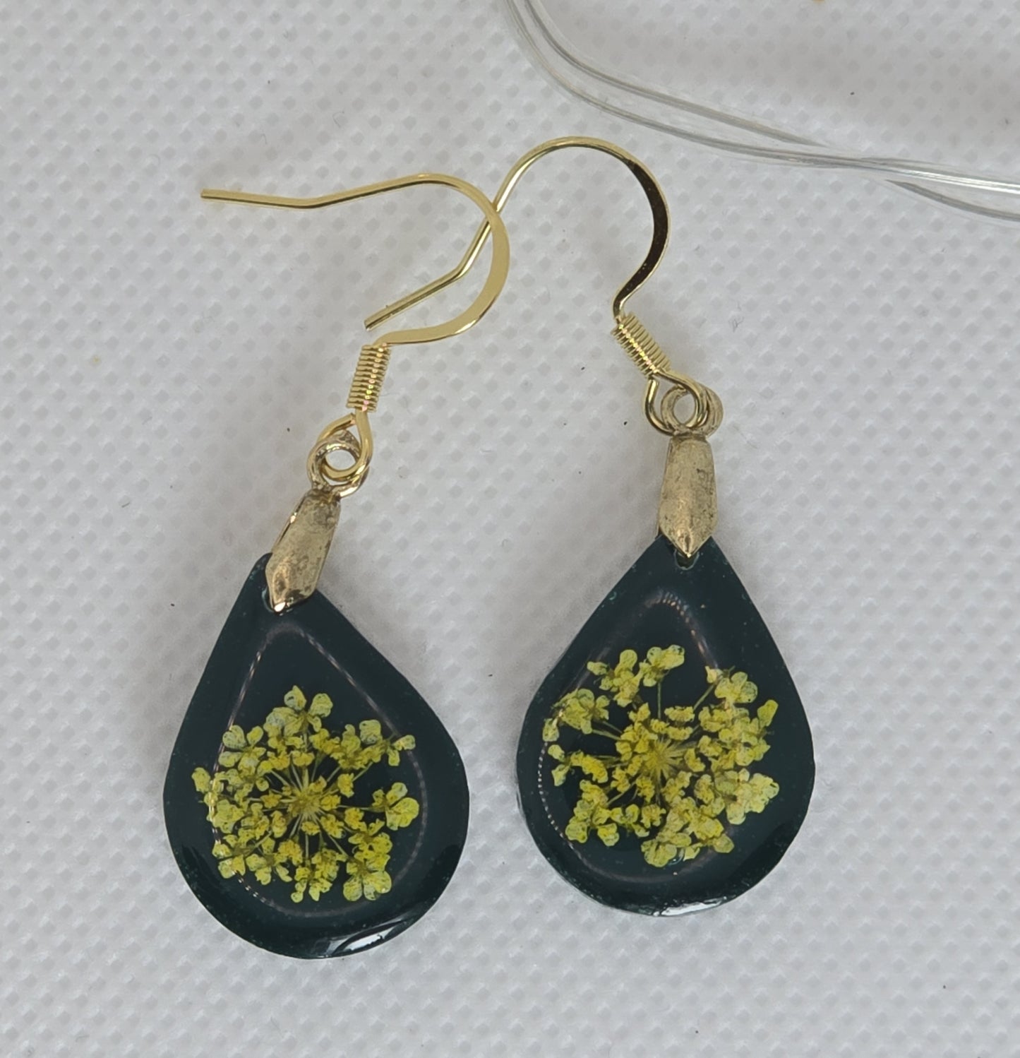 Earrings: deep green acrylic resin earrings in a teardrop shape containing a bouquet of yellow Queen Anne lace flowers,