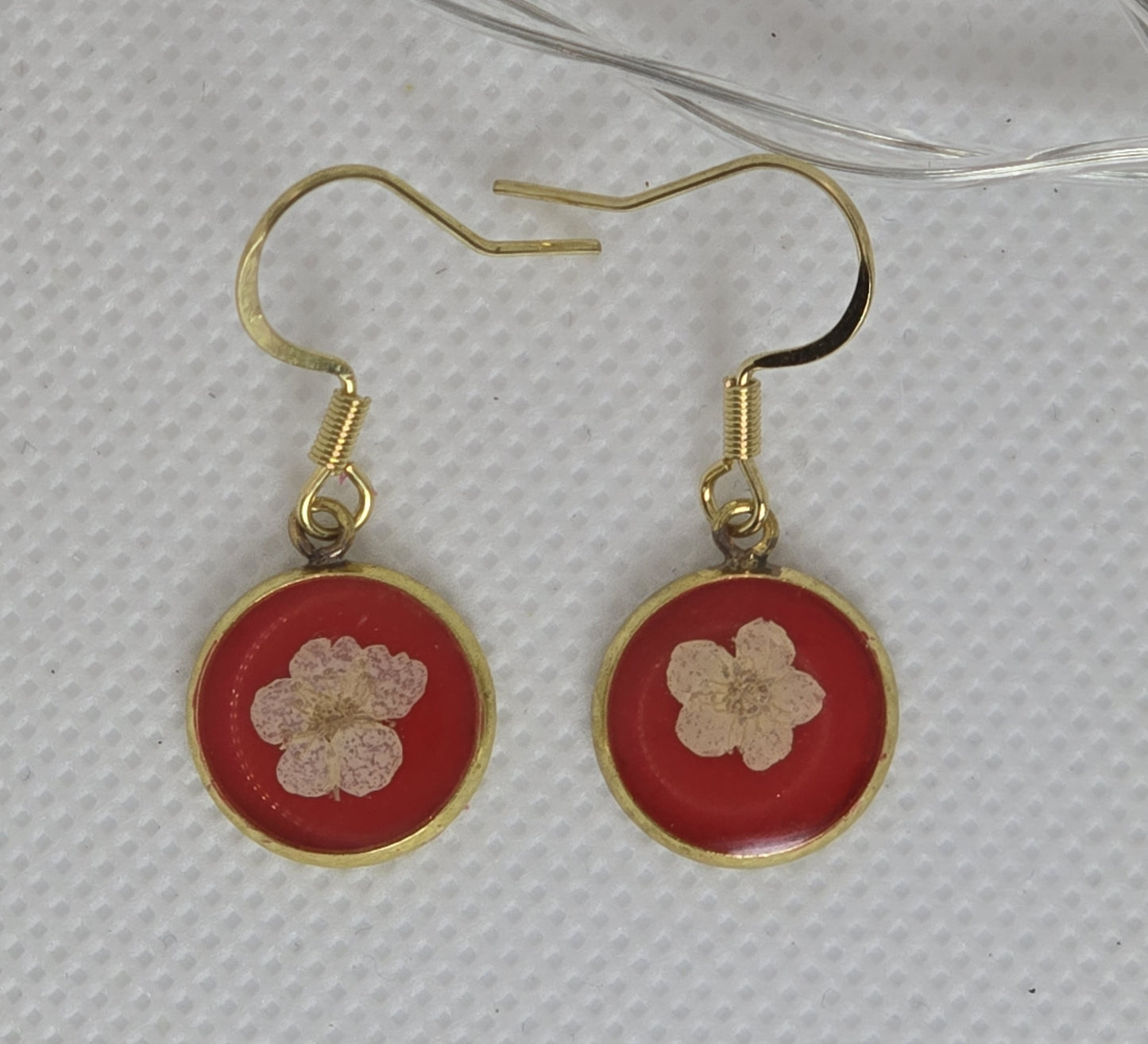 Earrings: Single white Alyssum flowers resting on beds of red acrylic resin, contained in a dainty round gold-coloured bezel