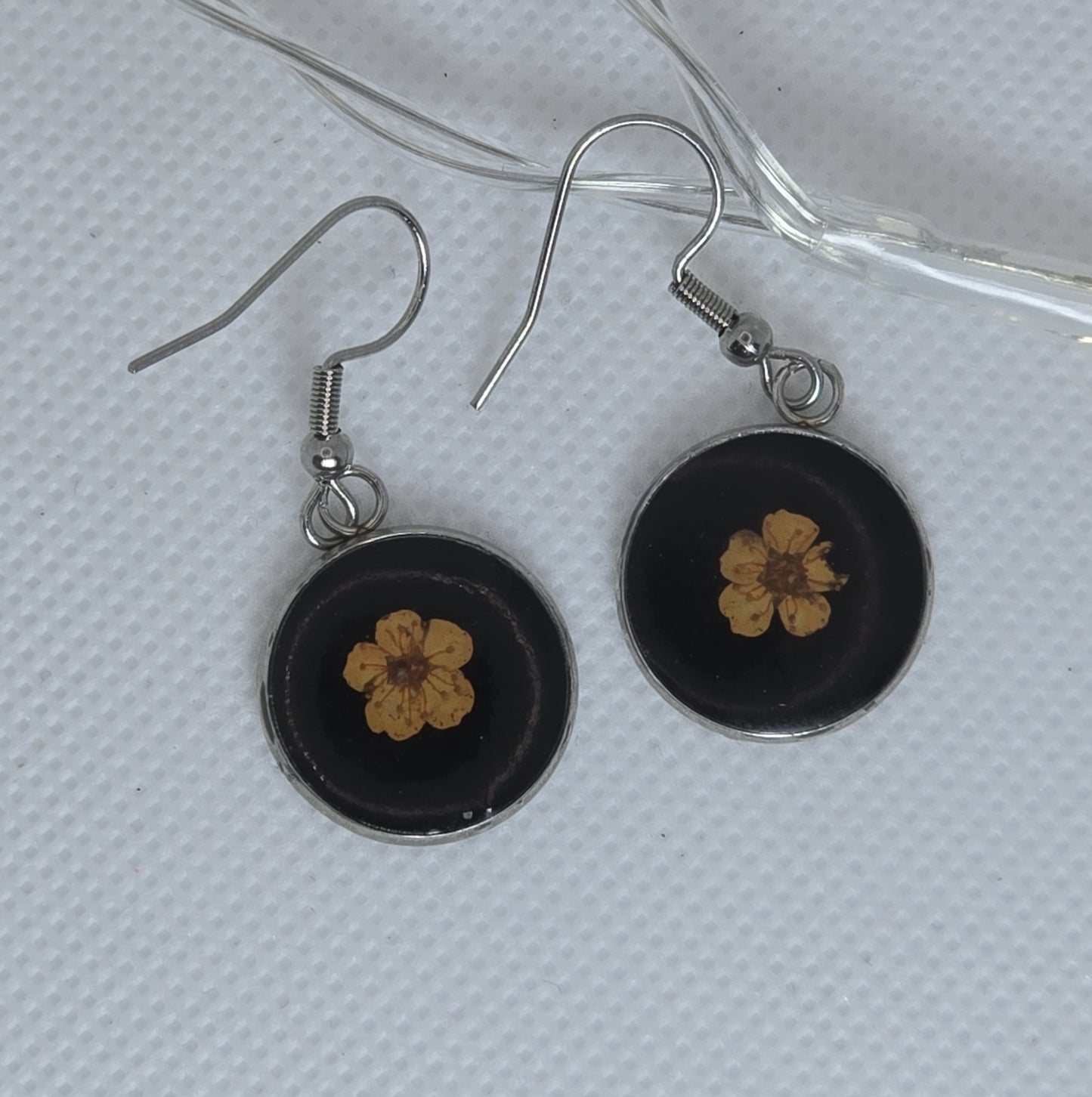 Earrings: Single orange Alyssum flowers resting on beds of black acrylic resin, contained in a round silver-coloured stainless steel bezel.