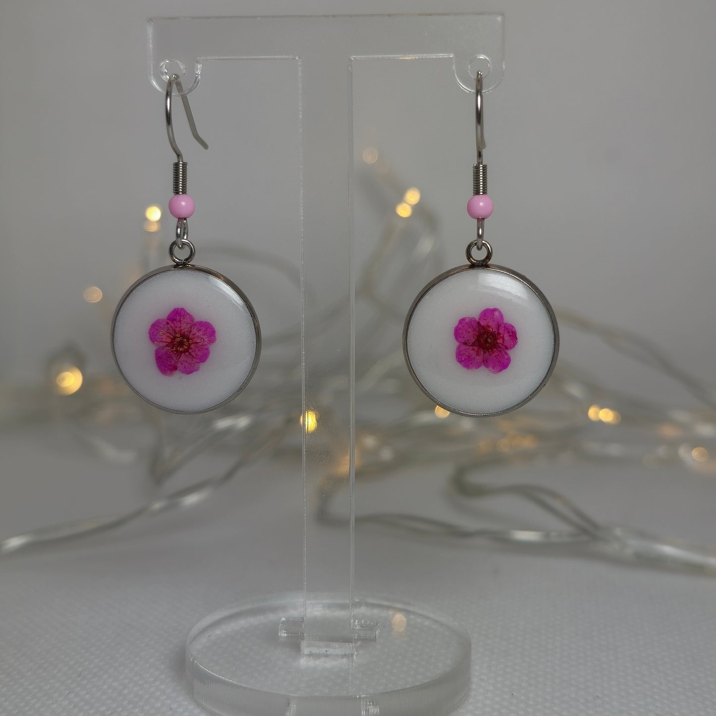 Single cerise pink Alyssum flowers resting on beds of white acrylic resin, contained a round silver-look stainless steel bezel.