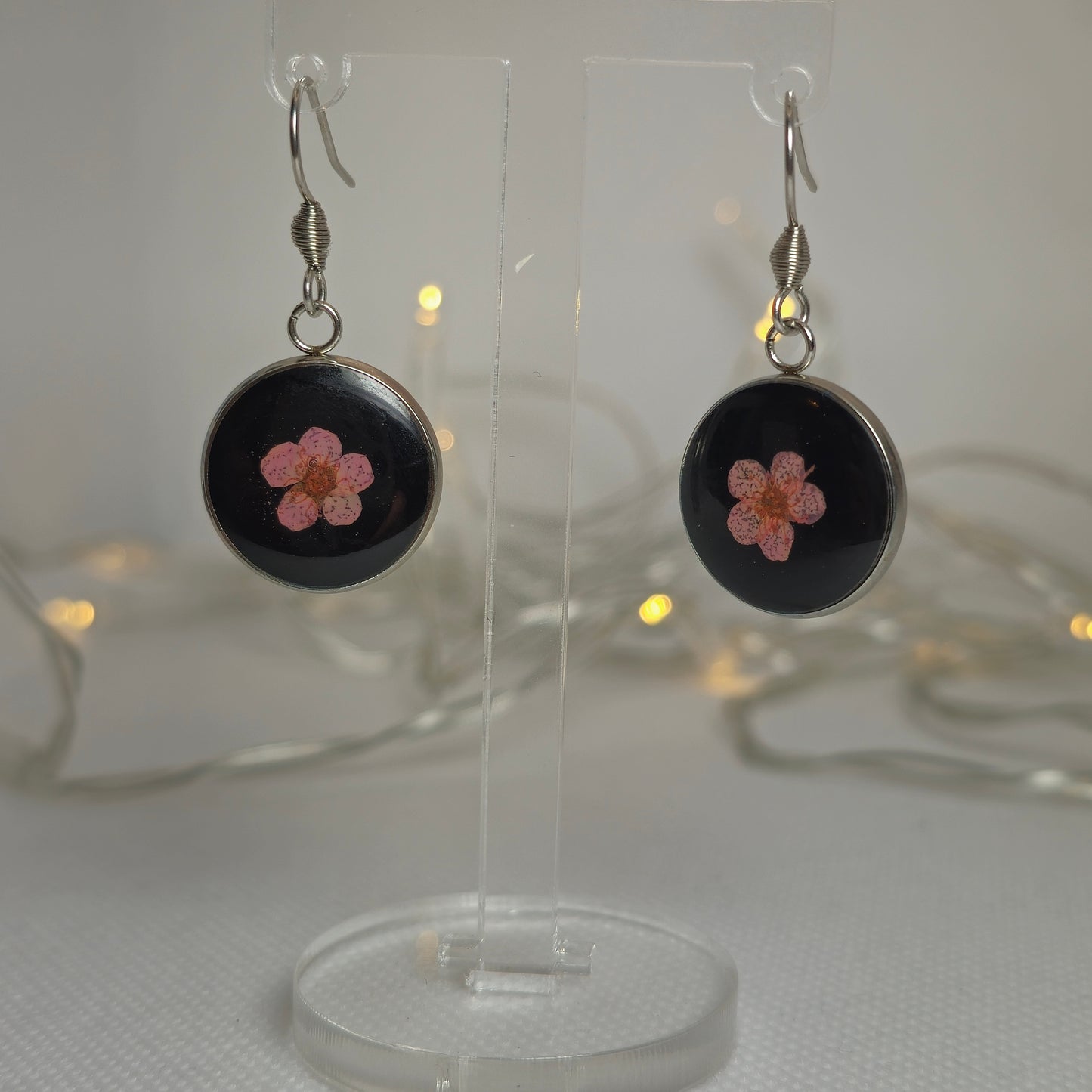 Earrings: single pink Alyssum flowers resting on beds of black acrylic resin, contained in a round silver-coloured stainless steel bezel.