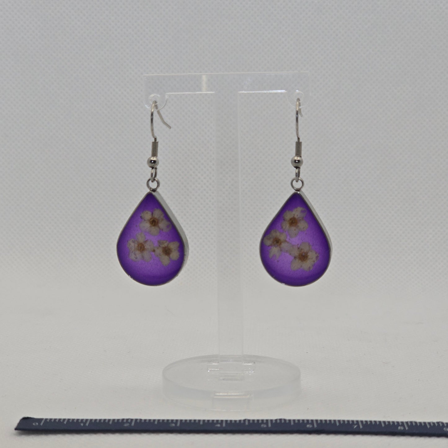 Earrings: silver-look teardrop shaped open bezel earrings with three white Alyssum flowers, set on a bed of translucent deep purple acrylic resin.