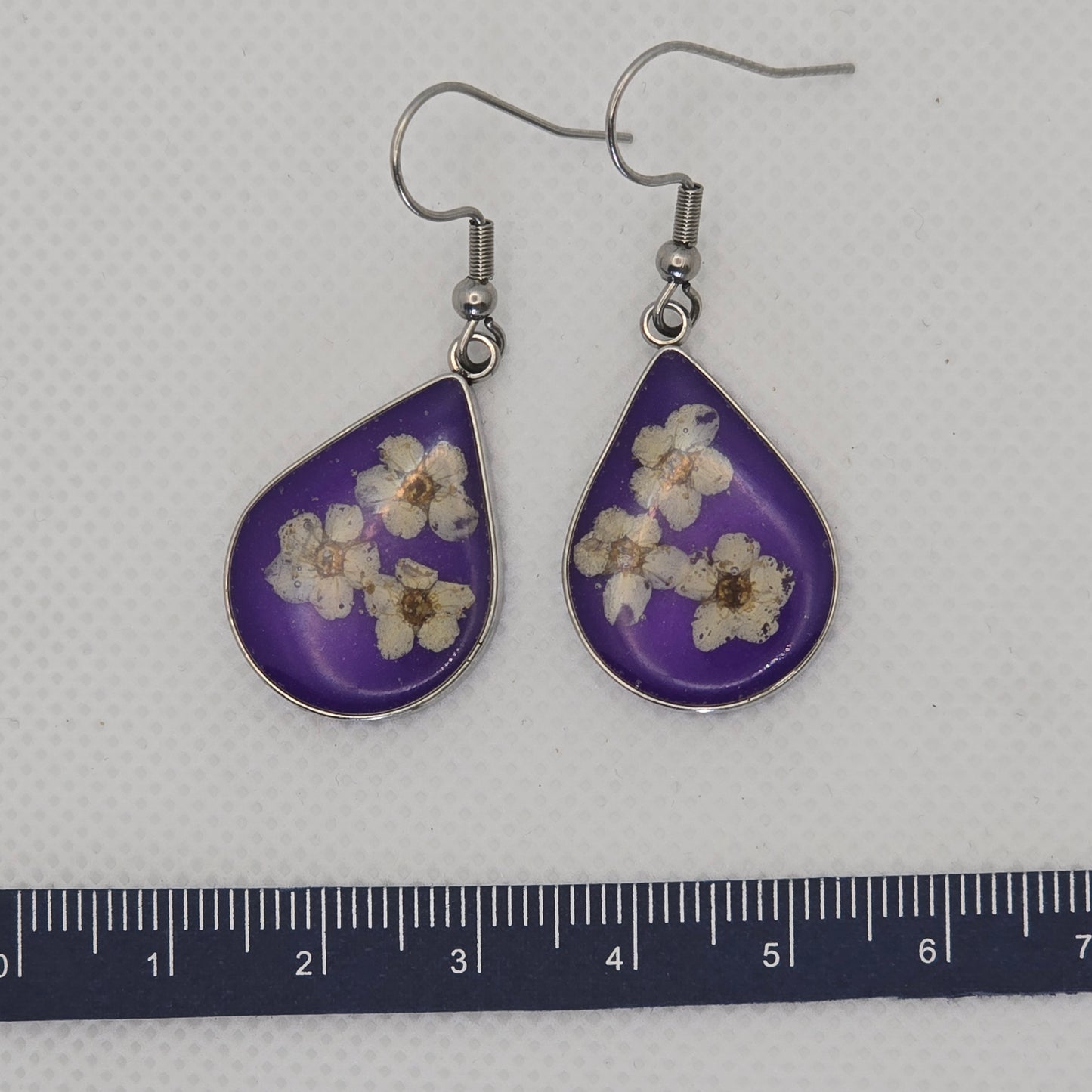 Earrings: silver-look teardrop shaped open bezel earrings with three white Alyssum flowers, set on a bed of translucent deep purple acrylic resin.
