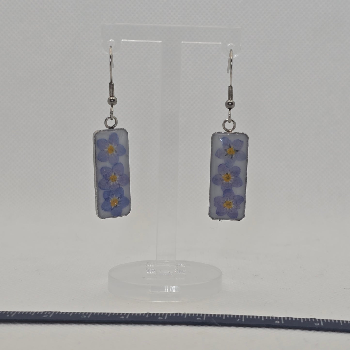 Earrings: Rectangular stainless steel tray-type bezel, filled with white acrylic resin on which three forget-me-not flowers are resting, domed in clear resin,