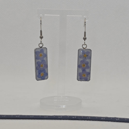 Earrings: Rectangular stainless steel tray-type bezel, filled with white acrylic resin on which three forget-me-not flowers are resting, domed in clear resin,